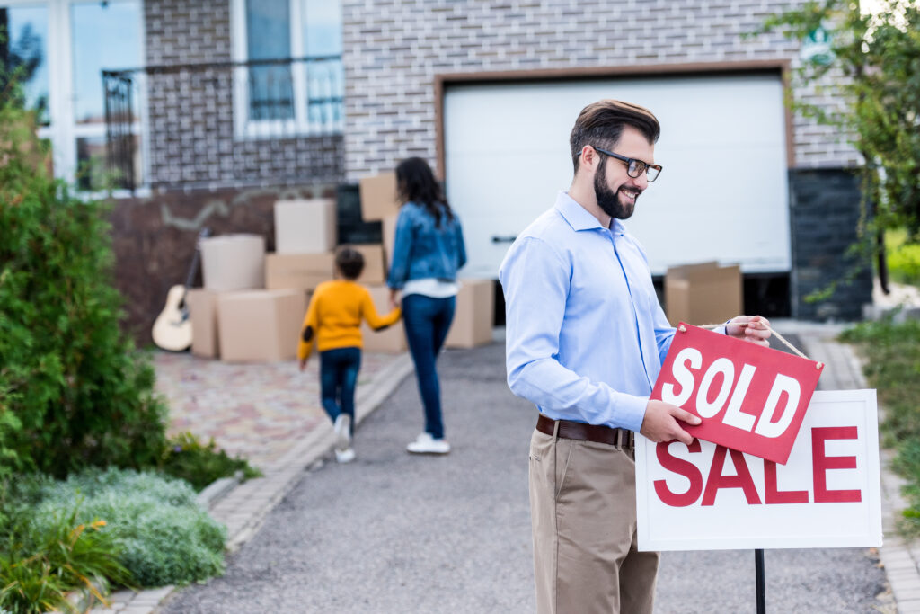 a man putting a sold sign over a sale sign after purchasing a house.