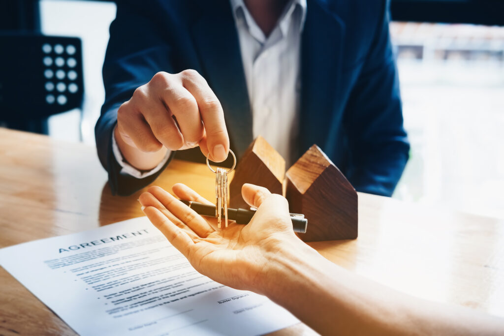 An image of a real estate agent handing keys to a buyer with an agreement on the table.