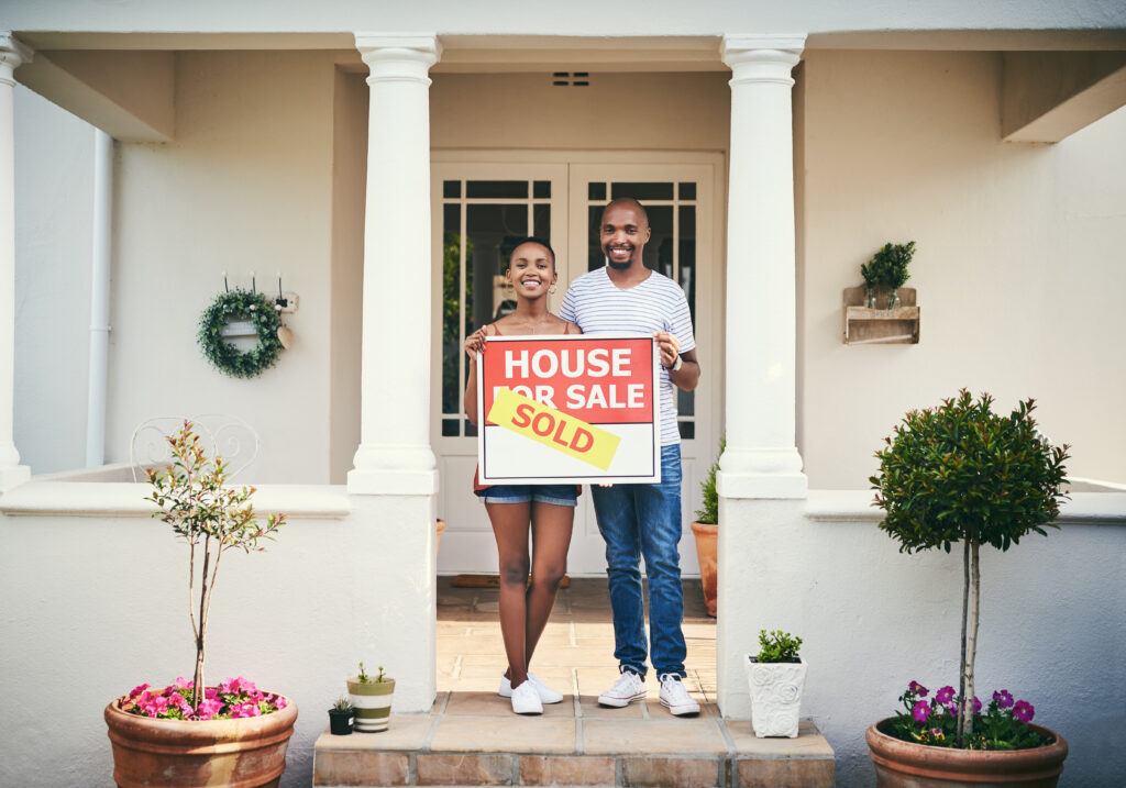 An image of a happy couple in front of their new home holding a sold sign.