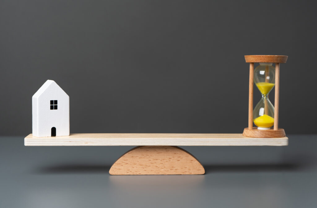 An image of a house and an hourglass sitting on opposite sides of a seesaw representing a successful real estate agent’s daily schedule.